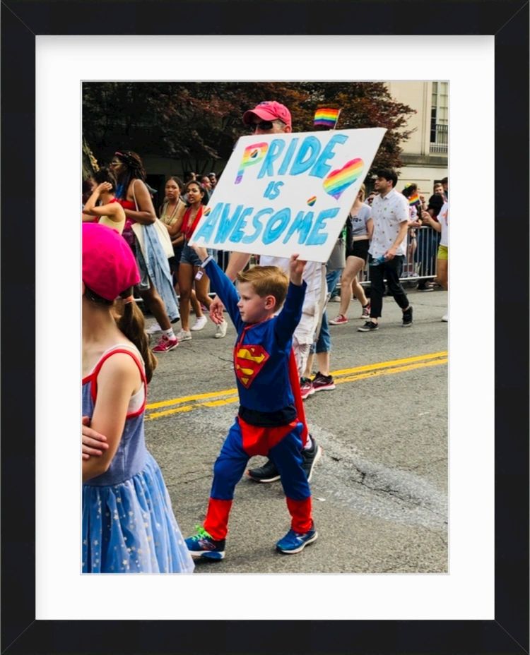 Boy in Superman costume holding pride sign in a black frame